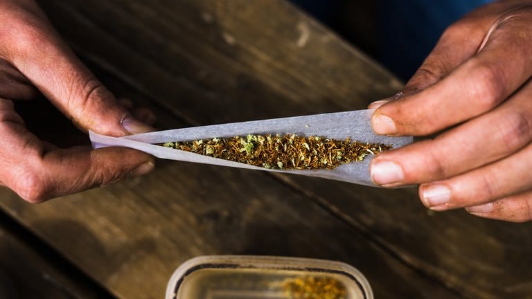 Ein Patient, mit der Erlaubnis Cannabis zu konsumieren, rollt einen Joint. Cannabis zu Hause oder gemeinschaftlich in speziellen Clubs anbauen oder ganz legal einen Joint rauchen - das soll mit dem Gesetz zur Cannabis-Legalisierung möglich werden.