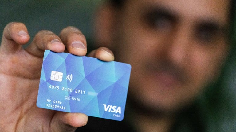 Ein Geflüchteter hält eine Debitcard in der Hand. Der Ortenaukreis hat bereits Mitte Januar die ersten Bezahlkarten für Geflüchtete ausgegeben.