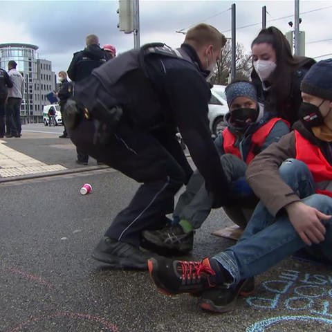 Polizisten tragen eine Klimaaktivisten von der Straße weg