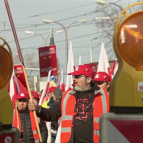 Demonstrierende Bauarbeiter in Warnwesten und mit Protestschildern