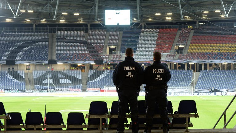 ARCHIV - Fußball, Länderspiel: Deutschland - Niederlande am 17.11.2015 in der HDI-Arena in Hannover (Niedersachsen). Zwei Polizisten stehen auf der Tribüne. Das Länderspiel Deutschland gegen die Niederlande ist wegen eines drohenden Sprengstoffattentats von Islamisten abgesagt worden. 