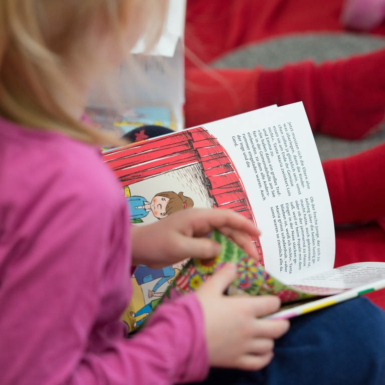 Ein Mädchen liest in einer Kita in einem Buch. (Foto: dpa Bildfunk, picture alliance/dpa | Daniel Reinhardt)
