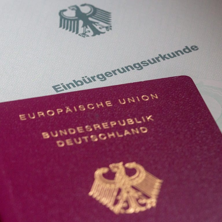 Eine Einbürgerungsurkunde der Bundesrepublik Deutschland und ein deutscher Reisepass liegen auf einem Tisch. 