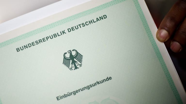 Ein Mann hält eine Einbürgerungsurkunde der Bundesrepublik Deutschland in der Hand. 