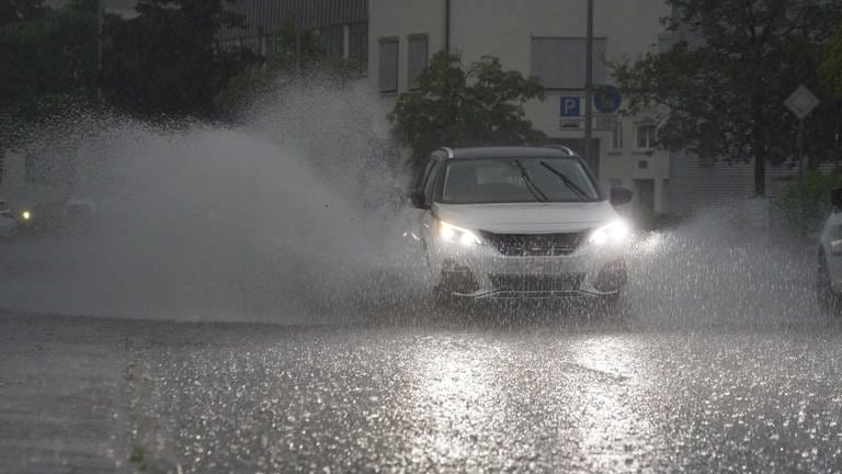 EIn Auto fährt bei Starkregen über eine regennasse Straße.