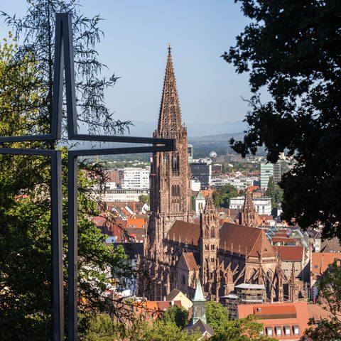 Ein stilisiertes Kreuz steht auf dem Freiburger Schlossberg während im Hintergrund das Münster zu sehen ist.