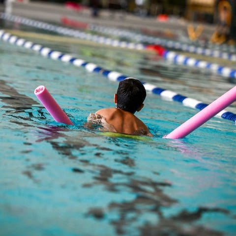 Ein Kind schwimmt mit einer Schwimmhilfe im Wasser.