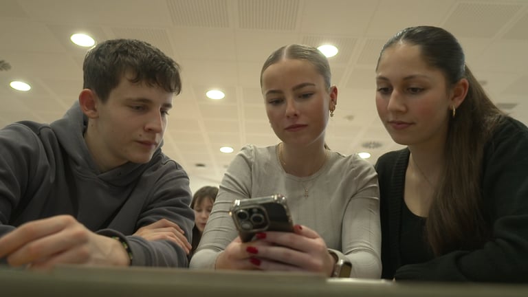 Drei Schüler schauen auf ein Smartphone.