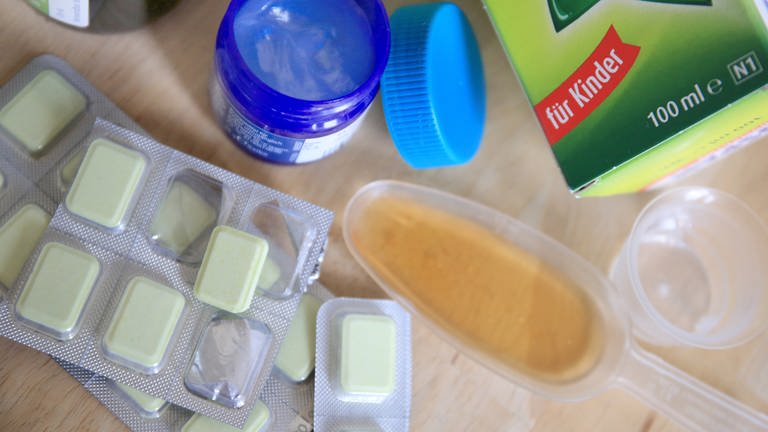 Medikamente wie Hustensaft, Lutschtabletten und Salbe stehen auf einem Tisch in einer Wohnung.