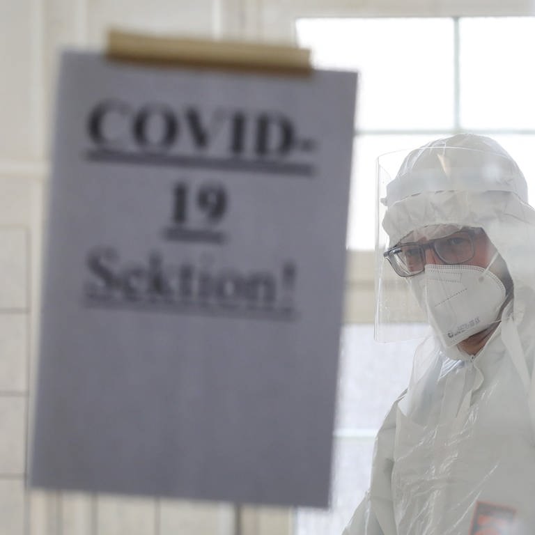 Johannes Manhart, Facharzt für Rechtsmedizin, steht hinter einer Tür im Sektionssaal der Universitätsmedizin, an der ein Zettel mit der Aufschrift "COVID-19 Sektion!" befestigt ist. Hier werden an Covid-19 Verstorbene obduziert, um die konkrete Todesursache festzustellen. 