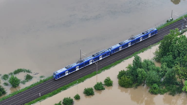 Ein Zug fährt über den höhrer gelegenen Bahndamm. Das Hochwasser des Flusses Schussen überschwemmt Teile von Meckenbeuren.