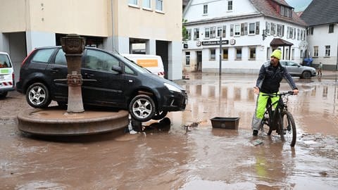 Auf einem Brunnen in Rudersberg steht ein durch ein Hochwasser weggespültes Auto. Seit Tagen kämpfen die Helfer in Bayern und Baden-Württemberg gegen die Flut und ihre Folgen.