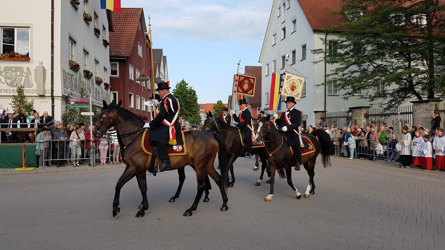 Reiter in Frack und Zylinder, sie tragen Fahnen. Im Hintergrund Häuser und Publikum (Foto: SWR, Friederike Fiehler)