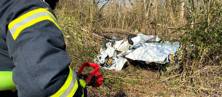 Feuerwehrmann vor Überresten von Flugzeug in einem Wald (Foto: Pressestelle, Feuerwehr Konstanz)