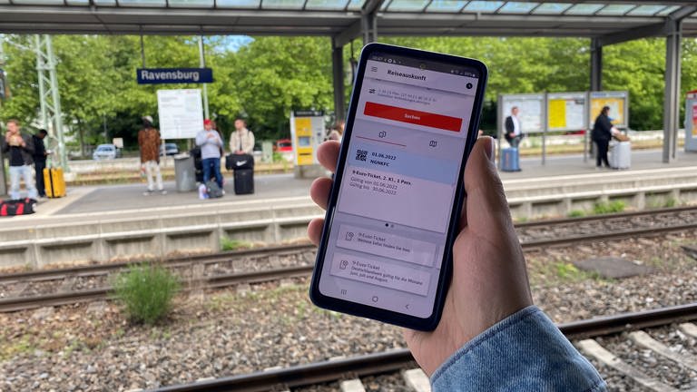 Seit Mittwoch gilt das 9-Euro-Ticket. Auf einem Handy ist die digitale Version zu sehen. Im Hintergrund der Bahnhof Ravensburg. (Foto: SWR, Thorben Langwald)