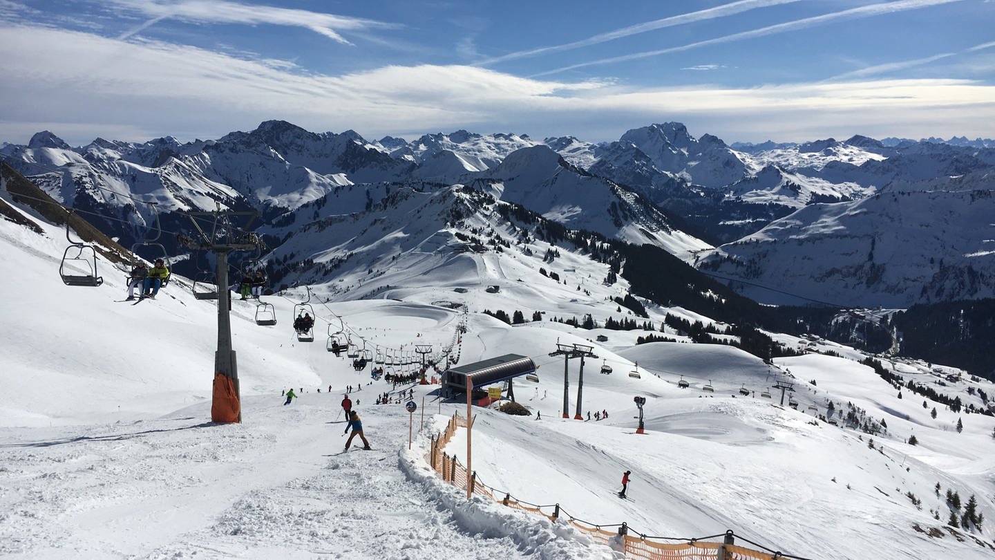 Skifahrer fahren im Skigebiet Damüls den Berg hinunter. Im Hintergrund sind schöne beschneite, weiße Berggipfel zu sehen. (Foto: SWR, Frederike Roser)