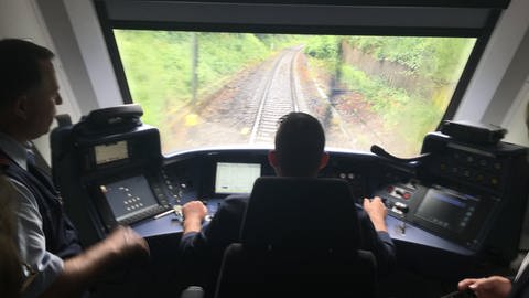 Ein Lokführer sitzt im Zug-Cockpit und steuert den Zug über die Schienen. (Foto: SWR)