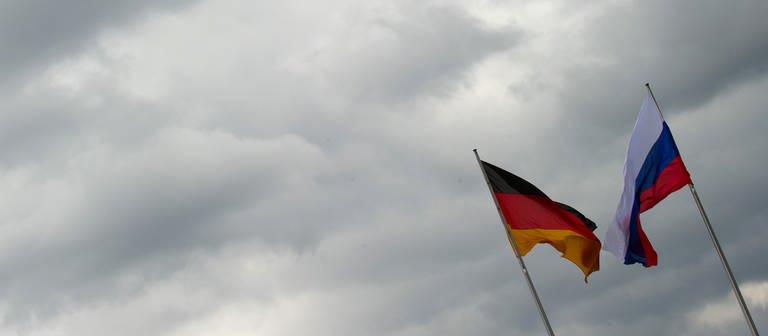Eine russische und eine deutsche Flagge wehen im Wind vor wolkenbedecktem Himmel.  (Foto: dpa Bildfunk, picture alliance/dpa/Tim Brakemeier (Symbolbild))