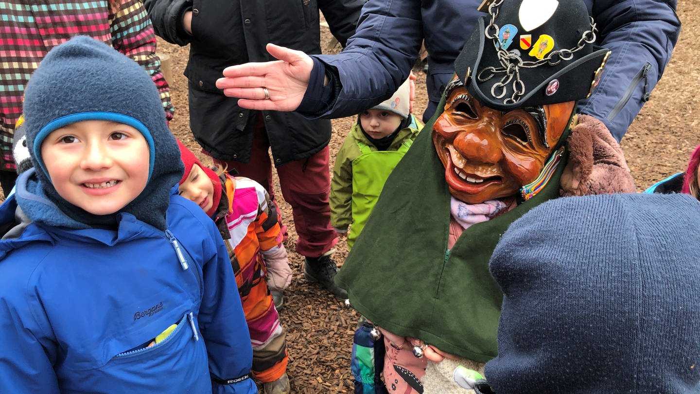 Kinder stehen beisammen. Eines hat eine Holzmaske des Göhrelöchners auf. Die Kinder strahlen. (Foto: SWR, Martin Hattenberger)