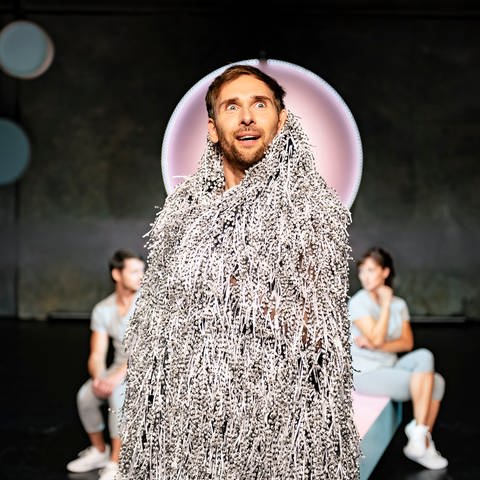 Ein Schauspieler hat einen silbernen Umhang aus einzelnen kleinen Lamettastückchen an. (Foto: Pressestelle, Ilja Mess)