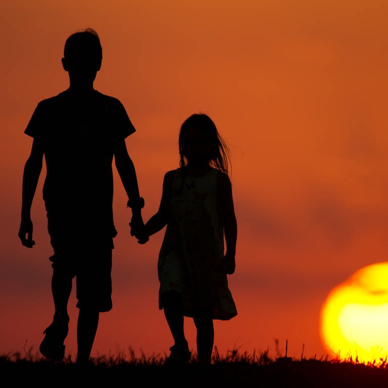 Zwei Kinder laufen Hand in Hand über eine Wiese.