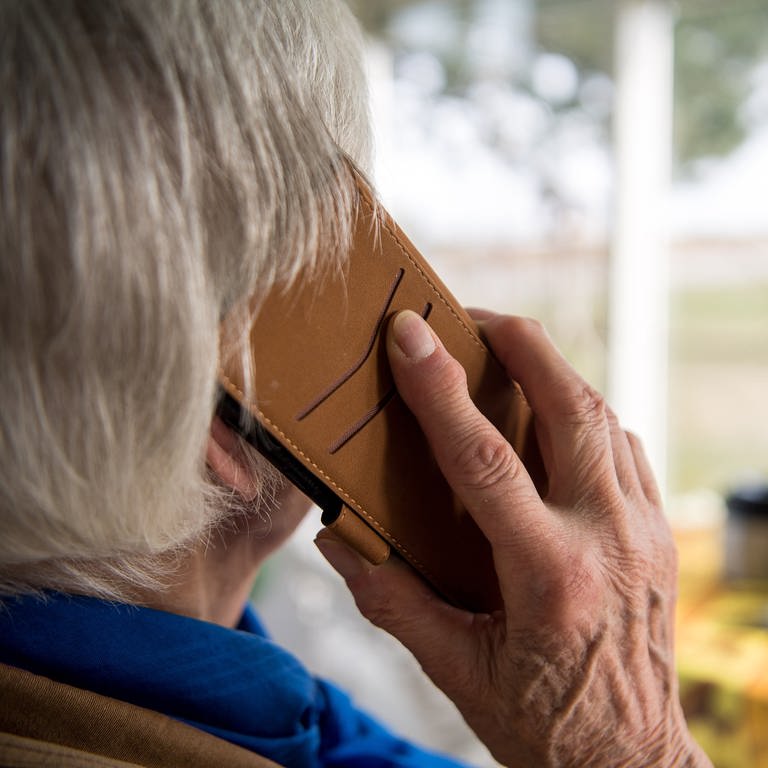 Eine Seniorin hält ein Telefon ans Ohr.