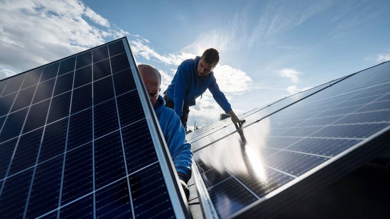 Arbeiter montieren eine Photovoltaikanlage auf dem Dach eines Wohnhauses