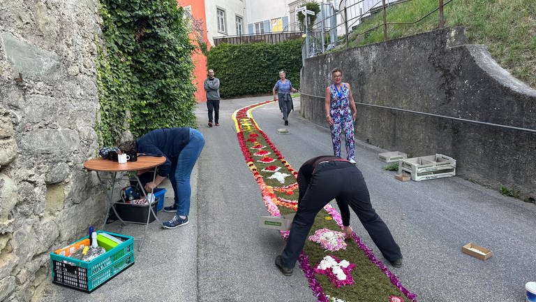 Mehrere Frauen und Männer stehen auf der Straße und legen einen Blumenteppich aus. (Foto: SWR)