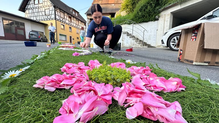 Ein junge Frau kniet auf der Straße und legt Blumen aus. (Foto: SWR)
