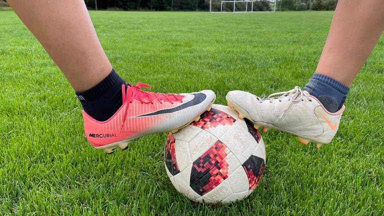 Die Füße zweier Fußballspielerinnen auf einem Ball.
