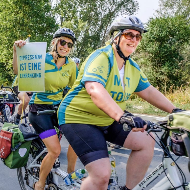 Zwei Radfahrerinnen in gelb-blauen Trikots auf einem Tandem.
