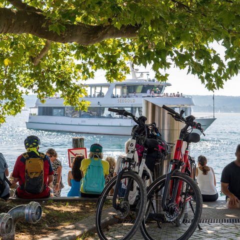In Überlingen am Bodensee machen Touristinnen und Touristen eine Pause am Wasser. Im Hintergrund ist das Passagierschiff MS Seegold zu sehen.