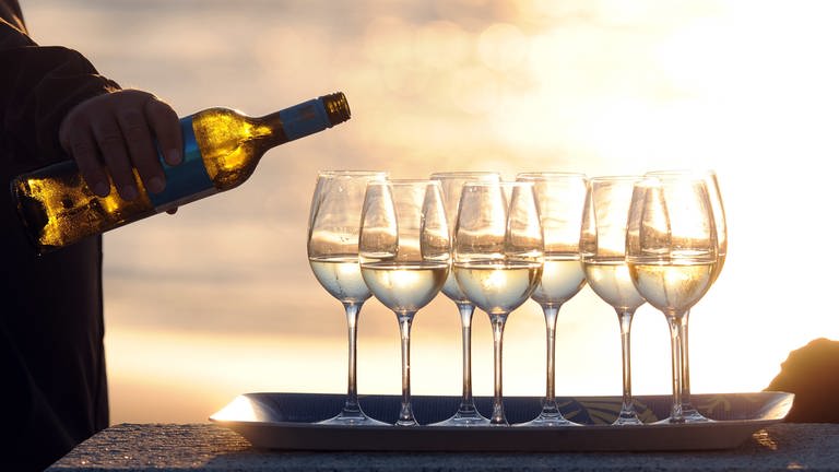 Weingläser und eine Hand mit einer Flasche Wein in Abendsonne, Symbolbild zu Veranstaltungstipps (Foto: dpa Bildfunk, Ingo Wagner)