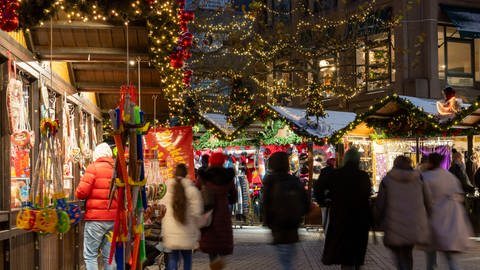 Menschen, unscharf dargestellt, schlendern über den Weihnachtsmarkt in Heilbronn, drum herum beleuchtete Buden (Foto: HMG/Jürgen Häffner)