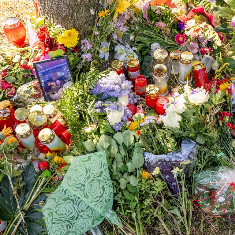 Blumen, Kerzen und Bilder liegen an einem Baum. Doppelgängerinnen-Mord.