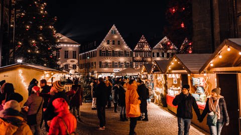 Menschen schlendern über den Öhringer Weihnachtsmarkt, rechts und links Buden, im Hintergrund beleuchtete Häuser (Foto: Stadt Öhringen)