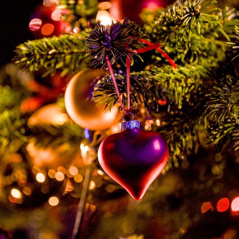 Ein Herzanhänger hängt an einem geschmückten Weihnachtsbaum. (Foto: dpa Bildfunk, Picture Alliance)