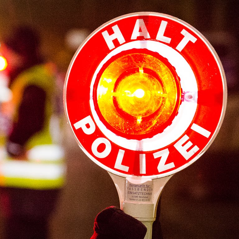  Ein Polizist hält bei einer Verkehrskontrolle eine rote Kelle mit der Aufschrift "Halt Polizei" hoch