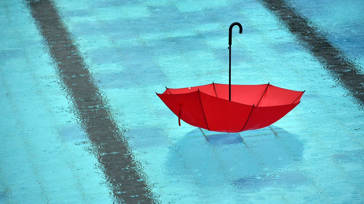 Bei strömendem Regen schwimmt ein Regenschirm im Freibad mit dem Griff nach oben in einem Becken. (Foto: picture-alliance / Reportdienste, picture alliance/dpa/dpa-Zentralbild | Ralf Hirschberger)