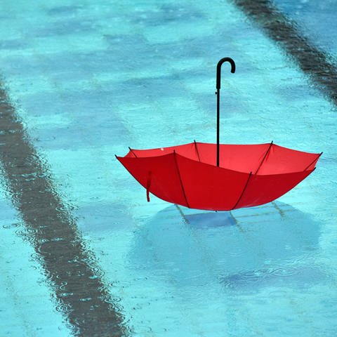  Bei strömendem Regen schwimmt ein Regenschirm im Freibad mit dem Griff nach oben in einem Becken.