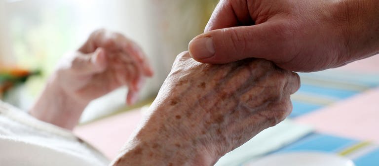  Ein Pfleger hält im Alten-und Pflegeheim die Hand einer Bewohnerin  (Foto: dpa Bildfunk, picture alliance / dpa | Oliver Berg)