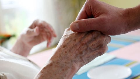  Ein Pfleger hält im Alten-und Pflegeheim die Hand einer Bewohnerin  (Foto: dpa Bildfunk, picture alliance / dpa | Oliver Berg)