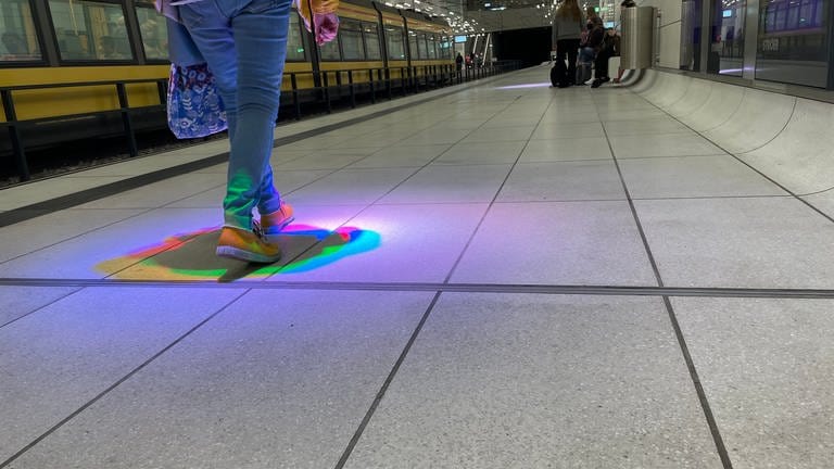 Wartende Fahrgäste werfen bunte Schatten, wenn sie unter einem bestimmten Licht-Spot am Bahnsteig stehen oder gehen. (Foto: SWR)