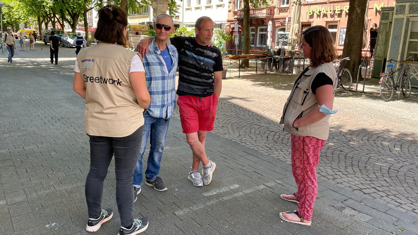 Streetworkerinnen der Diakonie sprechen auf dem Werderplatz in Karlsruhe mit zwei Männern