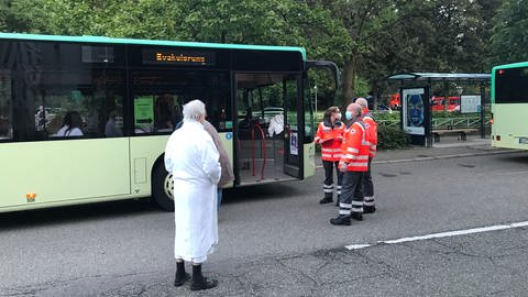 Ein Hotelgast im Bademantel steht vor einem Bus, in dem sich die Evakuierten des Badischen Hofs aufwärmen konnten (Foto: SWR)