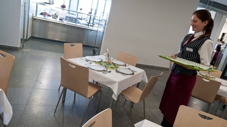 Auszubildende im Gastronomiegewerbe deckt Tische (Foto: IMAGO, viennaslide)