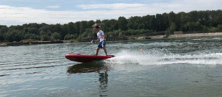 Surfer steht auf einem elektrisch betriebenen Surfbrett und fährt über einen See. (Foto: SWR)