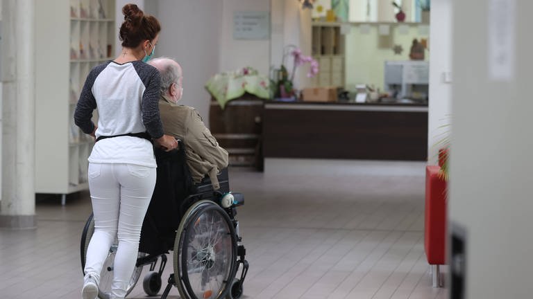 Pflegeheime kämpfen gegen die Ausbreitung des Corona-Virus. Pflegerin schiebt Mann im Rollstuhl.