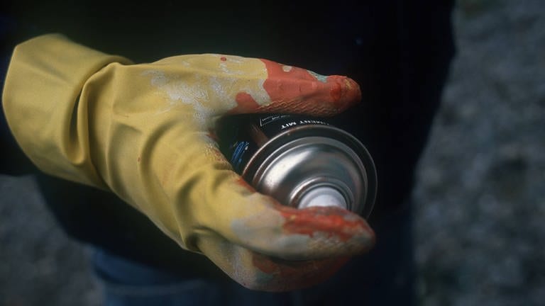 Mann hält Spraydose in der Hand, die in einem Gummihandschuh steckt. 