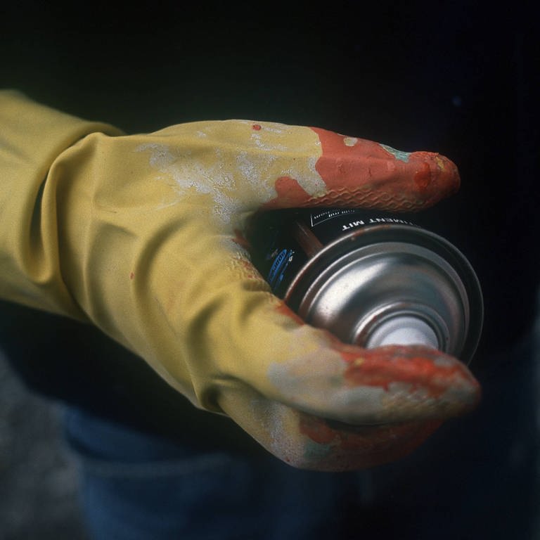 Mann hält Spraydose in der Hand, die in einem Gummihandschuh steckt.  (Foto: IMAGO, IMAGO / Jochen Tack)